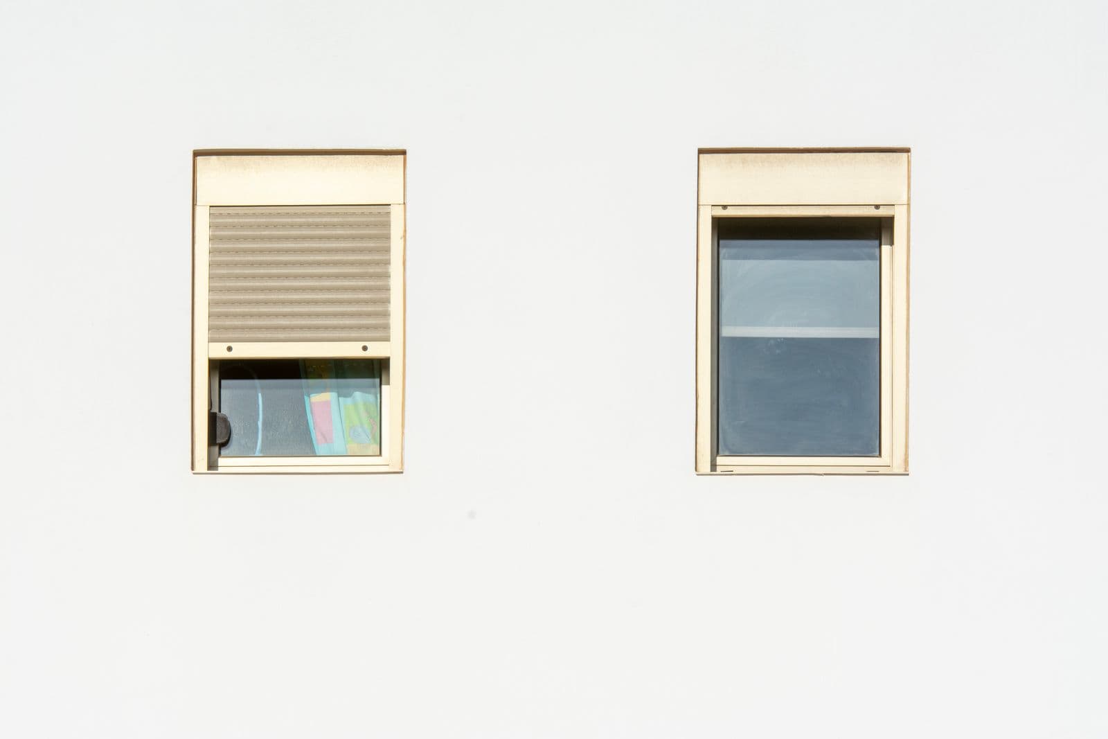 Schlichte weiße Fassade mit zwei Fenstern, eines mit heruntergelassenem Rollladen